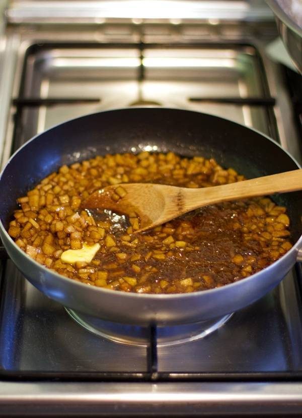 Apples cooking in a pan with a wooden spoon.