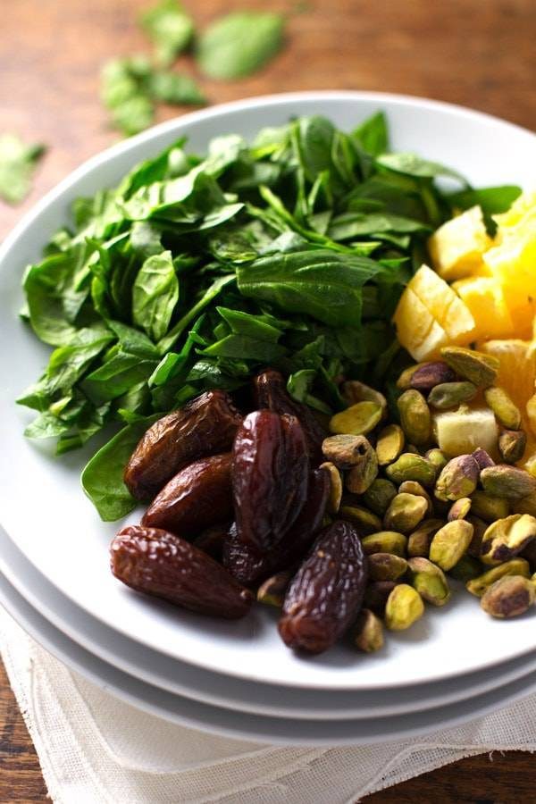 Dates, spinach, and pistachios on white plates.
