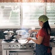 A woman cooking at a stove with a green hair net.