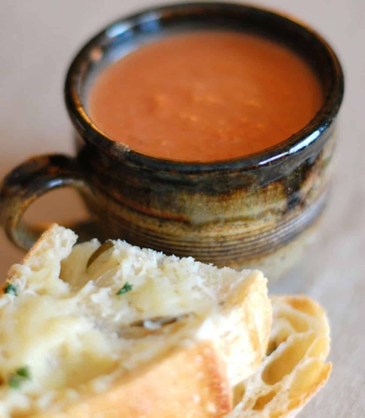 Creamy tomato balsamic soup in a mug with pieces of bread.