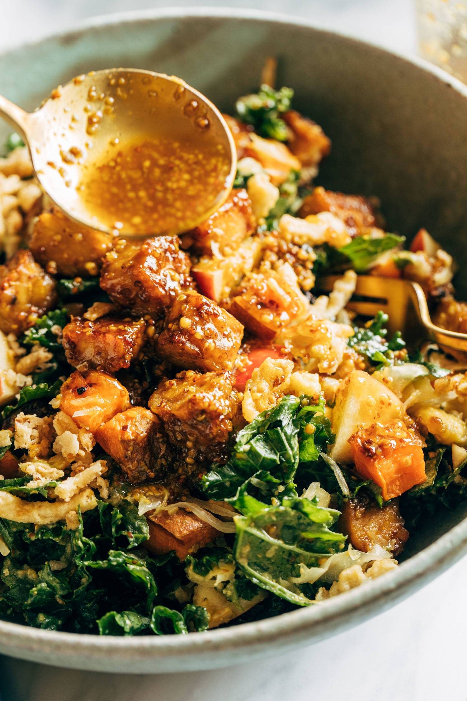 Dressing being poured on top of tempeh bowls with a spoon.